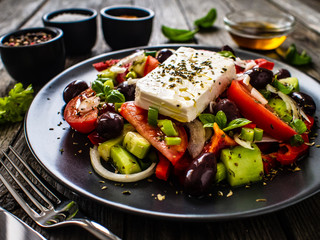 Fresh Greek salad - feta cheese, tomatoes, cucumber, red pepper, black olives and onion on wooden table
