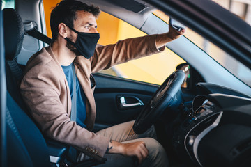 Fototapeta na wymiar A young man drives a car with a mask on his face, adjusts the view mirror, life during a pandemic caused by a virus