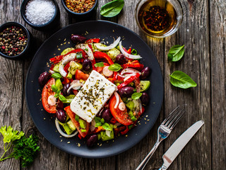 Fresh Greek salad - feta cheese, tomatoes, cucumber, red pepper, black olives and onion on wooden table
