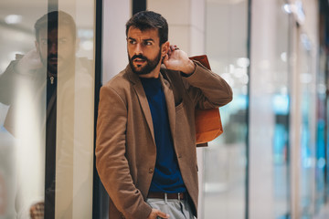 A man with bags in his hand stands next to the store and waits for his wife to leave the store, he has been waiting for a long time