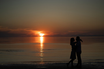 silhouette of a couple on the beach. Beautiful sunset of bright red orange color. Background for the travel website screensaver. Romantic picture, the concept of love.
