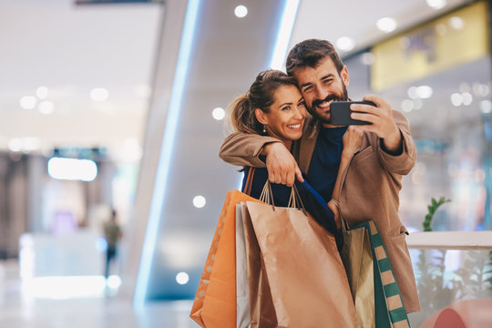 A couple satisfied with shopping is standing in the mall and taking photos of them