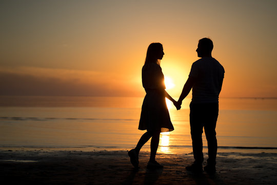 couple on the beach at sunset. Beautiful sunset of bright red orange color. Background for the travel website screensaver.