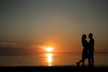 Fototapeta na wymiar silhouette of a couple on the beach. Beautiful sunset of bright red orange color. Background for the travel website screensaver. Romantic picture, the concept of love.