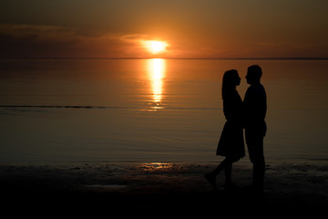 silhouette of a couple on the beach. Beautiful sunset of bright red orange color. Background for the travel website screensaver. Romantic picture, the concept of love.