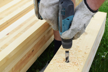 Closeup of worker hand drilling with wood drill bit drilling into natural wooden plank outdoors. Carpentry work and DIY concept.
