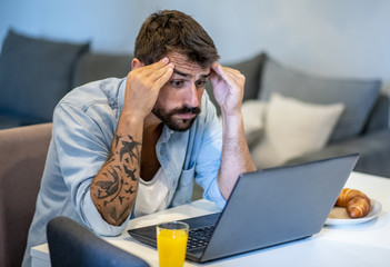 The husband is sitting alone at the laptop and trying to solve the problem with the bank, worried