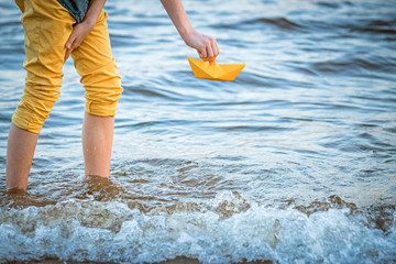 a boy launches a boat made of yellow paper into the sea, a symbol of travel, summer holidays, dreams of a cruise