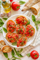Top view of traditional Italian appetizer, bruschetta with tomatoes and fresh basil on white plate top view