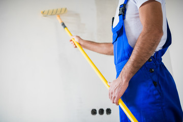 Close up, a man in overalls paints a wall in white with a roller