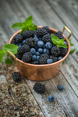 Ripe blackberries and blueberries in a vintage copper bowl. Selective focus.