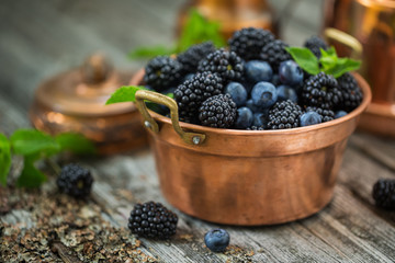 Ripe blackberries and blueberries in a vintage copper bowl. Selective focus.