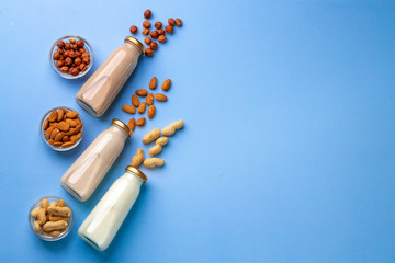 Bottles of vegan non dairy milk with various nuts on blue background