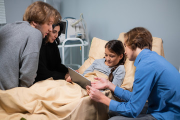 Obraz premium A sick kid in a hospital bed having visitors, the girl is listening to her brother attentively while he is teaching her to use a new app