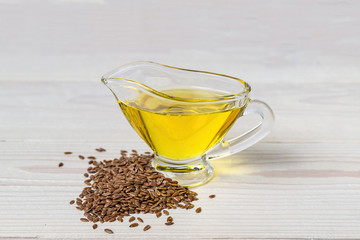 Flaxseed oil in a glass gravy boat. Flax seeds on a white background