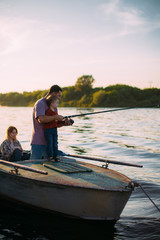 Young family fishing on boat on river in summertime. Father teaches son fishing. Photo for blog about family travel