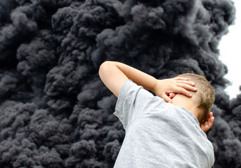 young boy covers his ears to protect hearing from explosion, large fire and dark smoke