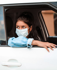 Beautiful young girl in a mask sitting in a car, protective mask against coronavirus, driver on a city street during a coronavirus outbreak, covid-19
