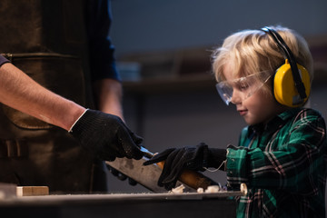 an experienced carpenter gives his little assistant carpentry tools in the workshop.