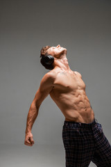 Cool young guy in wireless headphone listen to song, dance with naked torso on gray background....