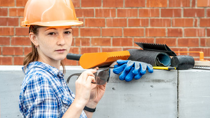 Woman in a hard hat on a building site against the background of a brick wall, aerated concrete blocks and construction tools. Concept of working in a non female profession