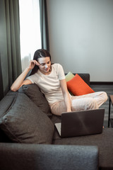 Obraz premium Young woman with modern laptop sitting on sofa at home