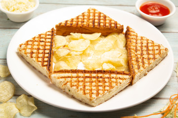 Cheese sandwich with potato chips, cheese, tomato, and lettuce served on wooden background.
