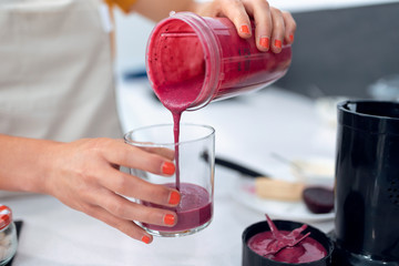 Young nutritionist woman serving healthy handmade smoothie in a cup in kitchen at home.