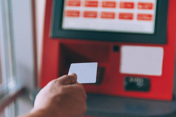Man holds a credit card against the background of an ATM machine.