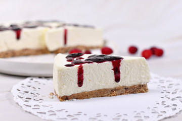 Slice of American cheesecae with red berry sauce on paper lace doily with cake and berris in burry...
