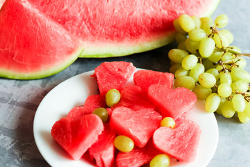 Fresh juicy watermelon slice with cut out heart shape, with fresh grapes, on plate, on concrete background