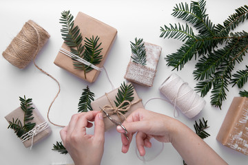 Christmas gifts wrapping ideas .Hand made gifts on white table with green decorations .Hands make...