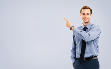 Portrait image of businessman showing something, standing over grey color background. Copy space area for some text. Success in business, job and education concept. Pointing confident man at studio.
