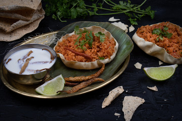 Tomato rice pilaf in papad bowl on banana leaf with chilies soaked in curd