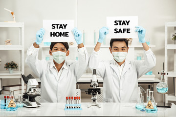 Two Male Scientists wear Face Mask in Lab while holding STAY HOME STAY SAFE paper.  SARS-CoV-2 , Covid-19 THEME