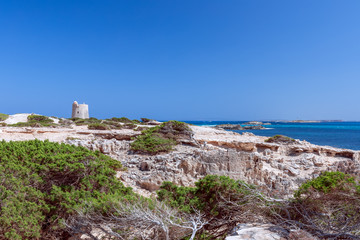 Fototapeta premium Beautiful view of the old observation tower (Torre De Ses Portes) and the rocky coast of the Ibiza island.