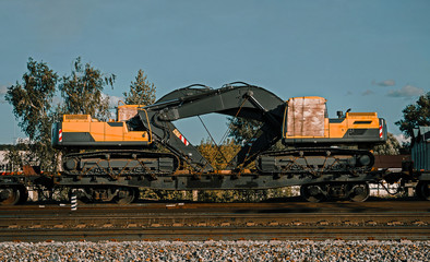 Two yellow excavators loaded onto a cargo railway platform. Logistics of delivery of the truck, transportation of heavy heavy machinery. Two heart-shaped buckets. Delivery of excavators to customers. 