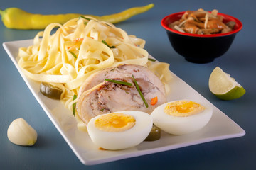 Noodles with pieces of meat and eggs in a white plate and dim sum with various traditional mushroom, soy and vegetable appetizers with chopsticks on a blue table. Asian food concept