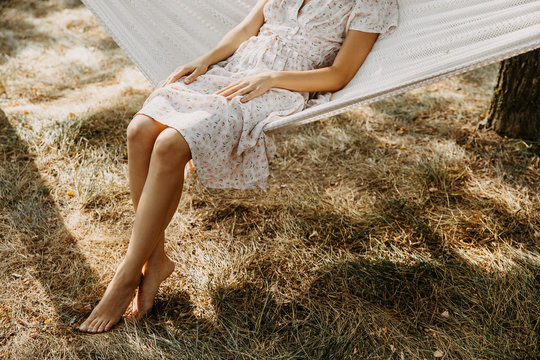 Legs of a barefoot woman sitting on hammock in the garden.