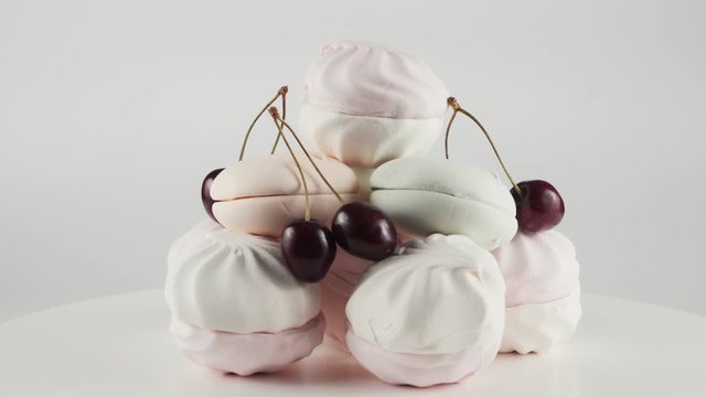 Close-up of coloured marshmallows and cherry at plate rotation over white colour background. Concept of candy bar, colourful sweets isolated. Copy space for your text or logo