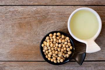 Soy bean oil with soybean seeds in black and white ceramics bowl isolated on rustic wood table background. Overhead view. Flat lay.