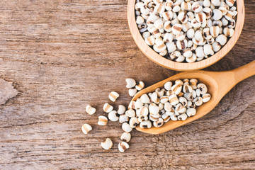 Closeup white Job's tears ( Adlay millet or pearl millet ) in wooden bowl and scoop isolated on old rustic wood table background background ,Top view. Flat lay