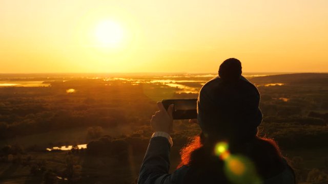 silhouette of a woman in sunshine, selfie, taking pictures at sunset, sunrise. Free Young girl tourist blogger records a selfie video on top of mountains using a smartphone with beautiful landscape.
