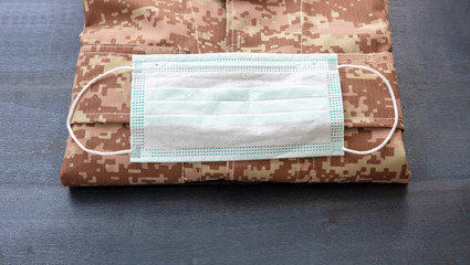 Coronavirus and USA army health care. Protective medical mask on a soldier uniform, wooden background