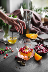 Fruit tea with honey in a large transparent teapot. Cranberries and lemons. Hot drink with pieces of fruit. Photo against a dark background.