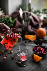 Fruit tea with honey in a large transparent teapot. Cranberries and lemons. Hot drink with pieces of fruit. Photo against a dark background.