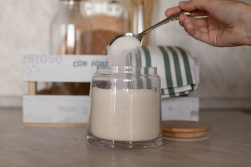 The girl spilled a spoonful of sugar into a jar