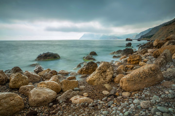 Sea beach and coastal stones in the water in the evening. Long exposure landscape.