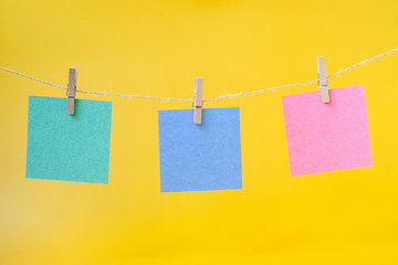 Paper cards of green, blue, pink color hanging on a rope on a yellow background. Concept.
