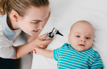 Smiling pediatrician doing ear exam with an otoscope to a baby at the hospital. Doctor examines infant baby 3-month-old